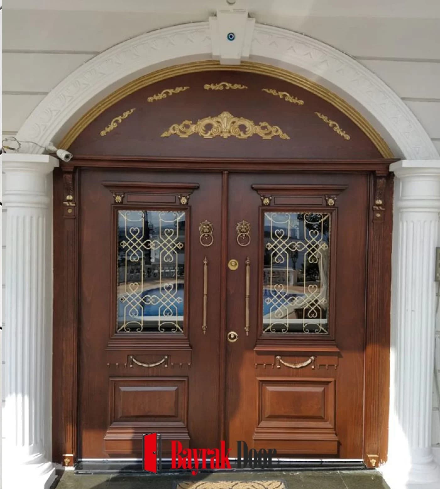 Oyma Kaset Ceviz Villa Kapısı BD-TR45 — Sütunlu kemerli alınlık altında mavi ferforje vitraylı ceviz çift kanat